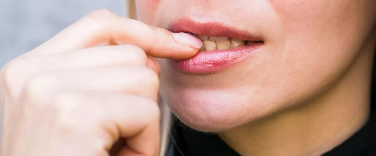 Candidiasis oral síntomas y tratamientos Primer plano de una mujer tocándose el labio y la comisura de la boca, ilustrando la irritación y malestar típicos de la candidiasis oral y los hongos en la boca.